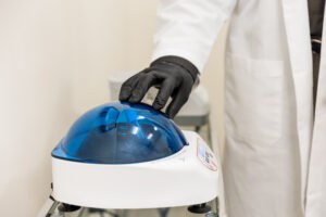 Enrichment Skin Solutions co-founder Michael Johnson, wearing a white lab coat and black gloves, stands over a centrifuge. This device rapidly spins blood for both PRF and PRP for hair near Blaine.