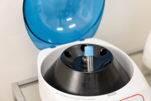 A close-up of an empty blood draw vial in a centrifuge with a transparent blue lid. Enrichment Skin Solutions medical providers rapidly spin blood to harvest PRP and PRF for ezGEL near Maple Grove.